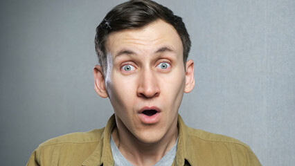 Amazed man shocked, saying WOW. Handsome guy with stylish hairdo surprised to camera over grey background.