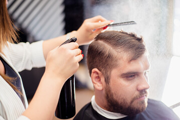 Canvas Print - Hairdresser woman doing hairstyle to bearded man in barbershop