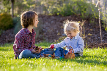 Cute children, eating chocolate bunnies and fighting with easter eggs after egg hunting in garden