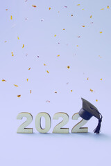 Graduation 2022 wearing graduate hat on a wooden 2022 number on very threaded colored background with flying confetti