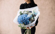 Very nice young woman holding big and beautiful bouquet of fresh hydrangea, delphinium, carnations, eucalyptus, brunia in blue colors, cropped photo, bouquet close up