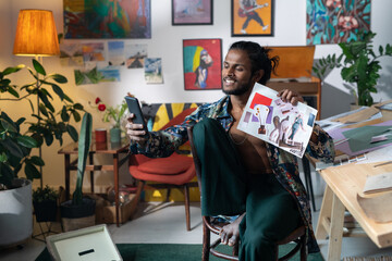 Portrait of modern young designer wearing casual clothes sitting on chair holding collage taking selfie on smartphone camera