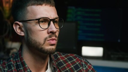 Angry hacker portrait. Irritated programmer close-up. Young man IT-specialist wearing glasses using laptop computer, having bad mood.