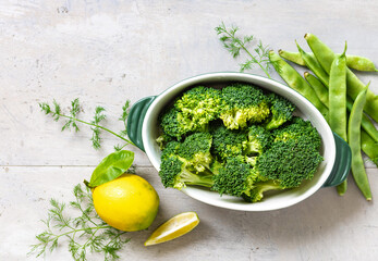 Poster - Raw ingredients for cooking healthy vegetarian food. Broccoli, green beans, lemon and parsley on light background top view copy space