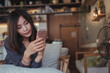 © Hand Robot - Beautiful Asian business woman holding smart phone and notebook while working in modern cafe with green vertical garden background