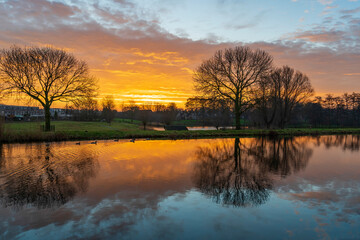 Wall Mural - The intense colors in the sky during this sunrise on a cold winter morning are beautifully reflected in the smooth water of the canal