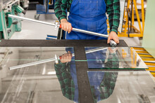 Glazier Standing Over A Cut Glass Pane With Specialized Cutting Equipment, Cutting Glass Panels In The Factory