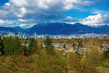 Wall Mural - Aerial view of downtown of Vancouver and seaport  with the Rocky Mountains mountain range and stormy sky in the background and cityscape with green trees in the foreground