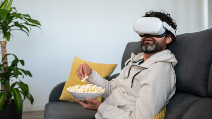 Man sitting on divan and enjoying virtual reality glasses while eating popcorn