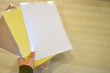 Worker grabbing some laminating pouches with yellow, craft and white sheets inside the plastic, and blank space on the right.