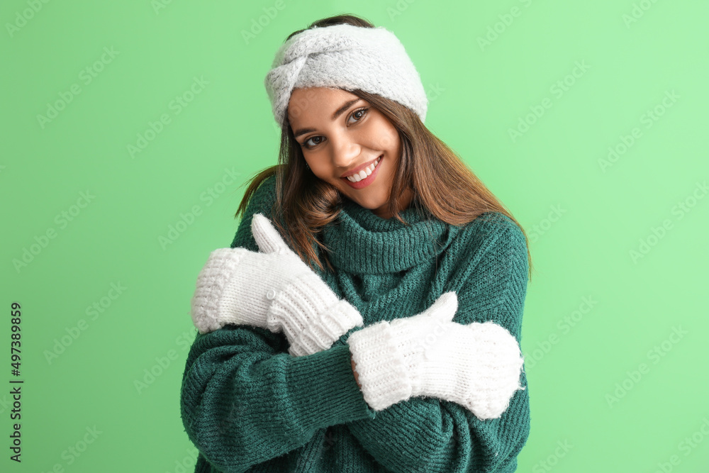 Young woman in warm gloves hugging herself on green background