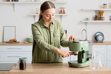 Canvas Print - Young woman making tasty coffee in kitchen