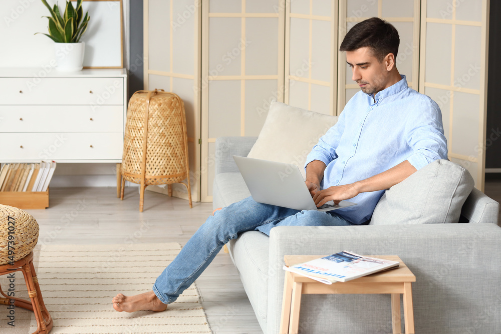 Young barefooted man using laptop on sofa at home