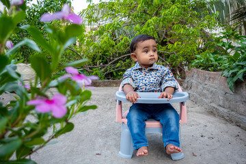 Wall Mural - T-shirt and jeans pants Wearing an infant sitting in a chair in the green garden. Baby's beautiful face on a beautiful afternoon. Asian cute baby boys portrait on rooftop.