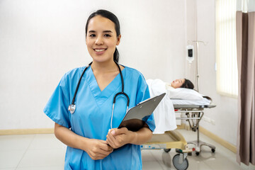 Portrait of confident smiling asian female doctor, nurse in standing smiling in a blue lab shirt holding patient documents in hand with stethoscope,  Health care concept