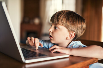 Wall Mural - Immersed in media. Shot of an adorable little boy using a laptop at home.