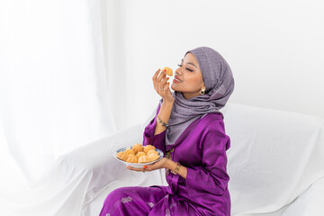 Muslim girl celebrates end of Ramadan, in purple kebaya dress with hijab, and holding bahulu food, white background, portrait waist up