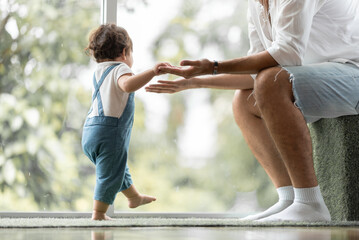 Wall Mural - cute toddler little child family concept, baby learning to walk with father and mother to help care and holding hand, first step with childhood parent support, small love portrait little boy at home