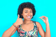young woman with afro hairstyle in sportswear against blue background holding an invisible braces aligner and rising thumb up, recommending this new treatment. Dental healthcare concept.