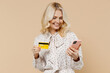 © ViDi Studio - Happy elderly gray-haired blonde woman lady 40s years old wear pink dress using mobile cell phone hold credit bank card doing online shopping isolated on plain pastel beige background studio portrait