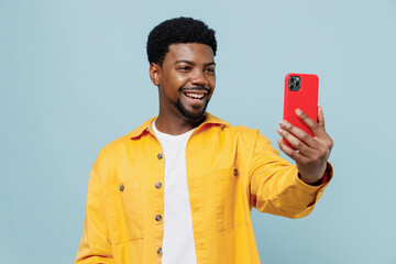 Wall Mural - Young happy man of African American ethnicity 20s wear yellow shirt doing selfie shot on mobile cell phone post photo on social network isolated on plain pastel light blue background studio portrait