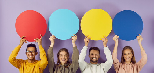 Colored round speech bubbles with copy space in hands of happy young people on purple background. Multiracial people hold blank mock up over their heads for dialogue, promotion, advertising or offers.