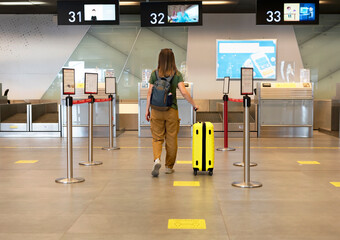 rear view of Young woman traveler in casual clothes with backpack carrying yellow suitcase at the check-in desk at airport terminal tourism concept of air flights travel and vacation