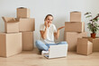 © sementsova321 - Positive smiling woman wearing t shirt and jeans sitting on floor surrounded with cardboard boxes and talking on phone, having no answer, being not sure, talking with client of real estate agency.
