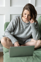 Wall Mural - Young beautiful smiling woman using laptop lying on the couch. Concept of freelance job, home office. Female using technology for learning, shopping, e-commerce, communication, social media