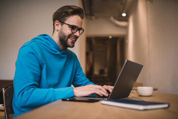 Happy Caucasian freelancer browsing web design on modern laptop computer, smiling IT professional in optical spectacles for provide eyes protection creating program code during remote working