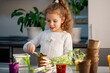 © Natalya Temnaya - A cute girl plants at home in eco pots. She is wearing a white sweater. The garden of the house. Hobby.