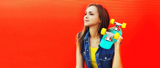 Wall Mural - Portrait of happy smiling young woman with skateboard wearing colorful on orange background