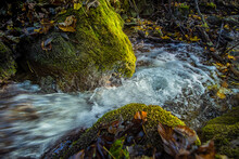 Photo Of A Water Stream Flowing Among Rocks Covered In Moss