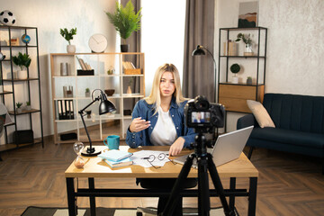 Attractive business woman in casual wear recording masterclass about success and finance. Pretty lady using modern laptop, camera for remote work. Freelancer girl making vlog