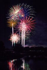 Canvas Print - Vibrant fireworks in the night sky reflected in a lake or a river