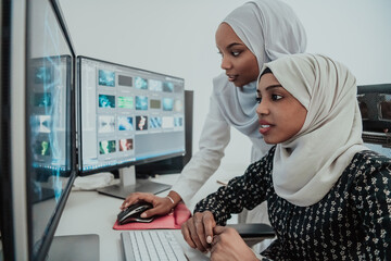 Friends at the office two young Afro American modern Muslim businesswomen wearing scarf in creative bright office workplace with a big screen