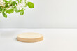 Empty round wooden podium for product presentation and spring flowers on a light background. Mockup concept with copy space