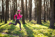Sporty young female wearing rose clothes runs at a sunny spring forest along the pathway