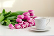 a white mug with a saucer and a bouquet of beautiful pink tulips