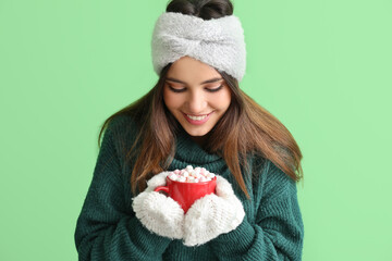 Wall Mural - Young woman in warm gloves with cup of cocoa on green background