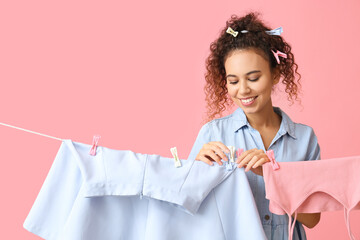 Wall Mural - Young African-American woman hanging clean skirt with clothespin on pink background