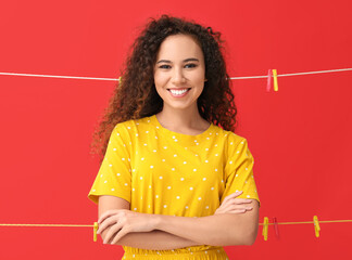 Wall Mural - Young African-American woman with hanging clothespins on red background