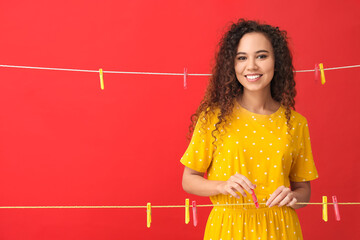 Wall Mural - Young African-American woman hanging clothespin on red background