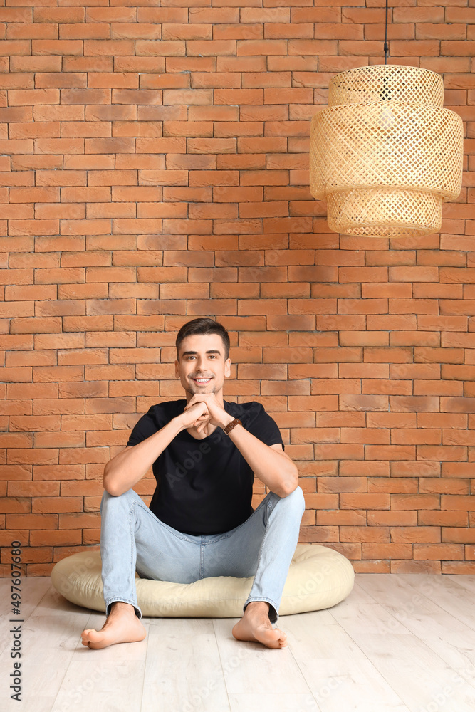 Young barefooted man sitting on pouf near brick wall