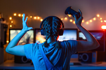 Wall Mural - A gamer or a streamer girl at home in a dark room with a gamepad playing with friends on the networks in video games. A young man sits in front of a monitor or TV.