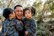 © Erin Brant/Stocksy - Asian dad holding daughters outdoors