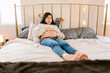 © ByLorena/Stocksy - Pregnant woman in bed using fetal heartbeat monitor