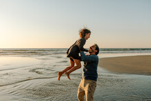 Father Lifting Daughter Into The Air At The Beach
