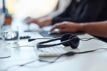 Aufkleber - Get the assistance you need. Shot of a set of headsets lying on a desk with workers sitting in the background.