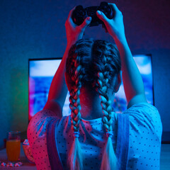 Wall Mural - Gamer or streamer girl at home in a dark room with a gamepad, playing with friends online in video games. with popcorn and multi-colored light. Background